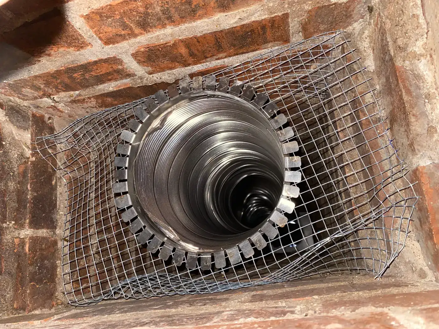 Stainless steel chimney liner installed in a brick flue with mesh screen